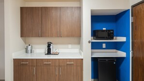 A compact kitchenette with wooden cabinets, a microwave, a coffee maker, and a small black refrigerator. - Holiday Inn Express & Suites N Waco Area - West by IHG (West)