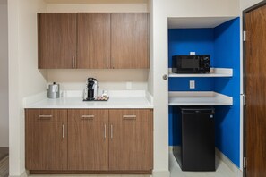 A compact kitchenette with wooden cabinets, a microwave, a coffee maker, and a small black refrigerator. - Holiday Inn Express & Suites N Waco Area - West by IHG (West)