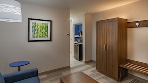 Une chambre d’hôtel avec un canapé bleu, un banc en bois, un tableau encadré au mur et une armoire.