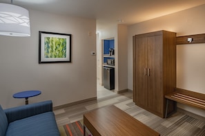 Une chambre d’hôtel avec un canap é bleu, un banc en bois, un tableau encadré au mur et une armoire.