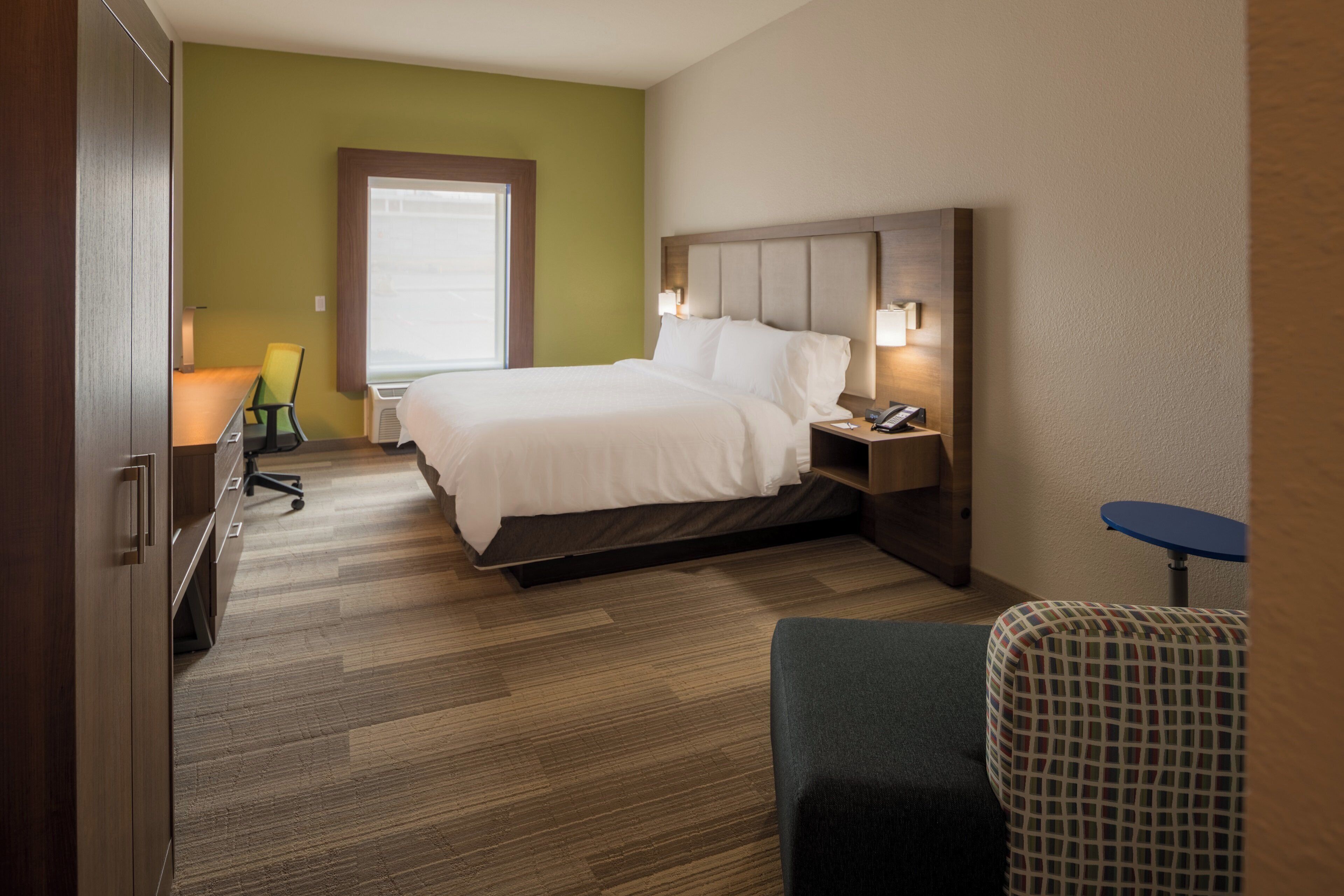 Quarto de hotel com cama, mesa de cabeceira, abajur, cadeira e escrivaninha com cadeira.