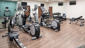 Une salle de sport équipée de divers appareils d’exercice, notamment des tapis de course, des vélos elliptiques et des poids libres.