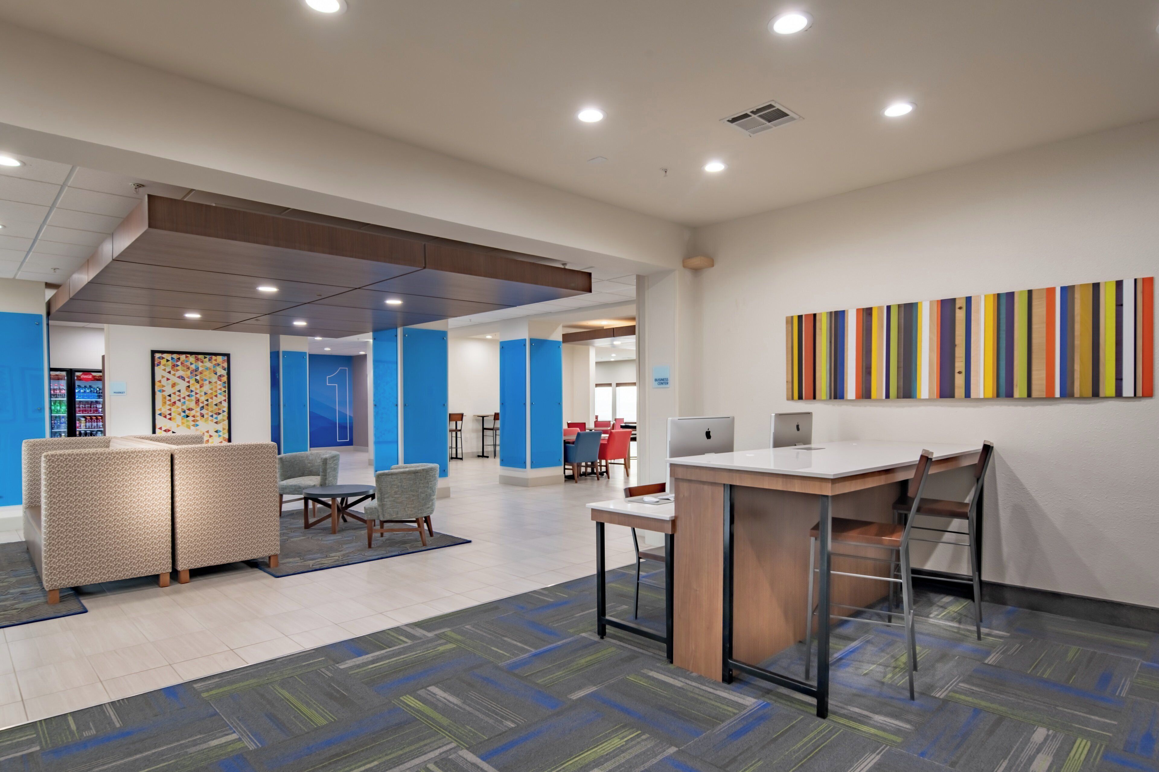 A modern office space with a meeting area, individual workstations, and a colorful abstract art piece on the wall.