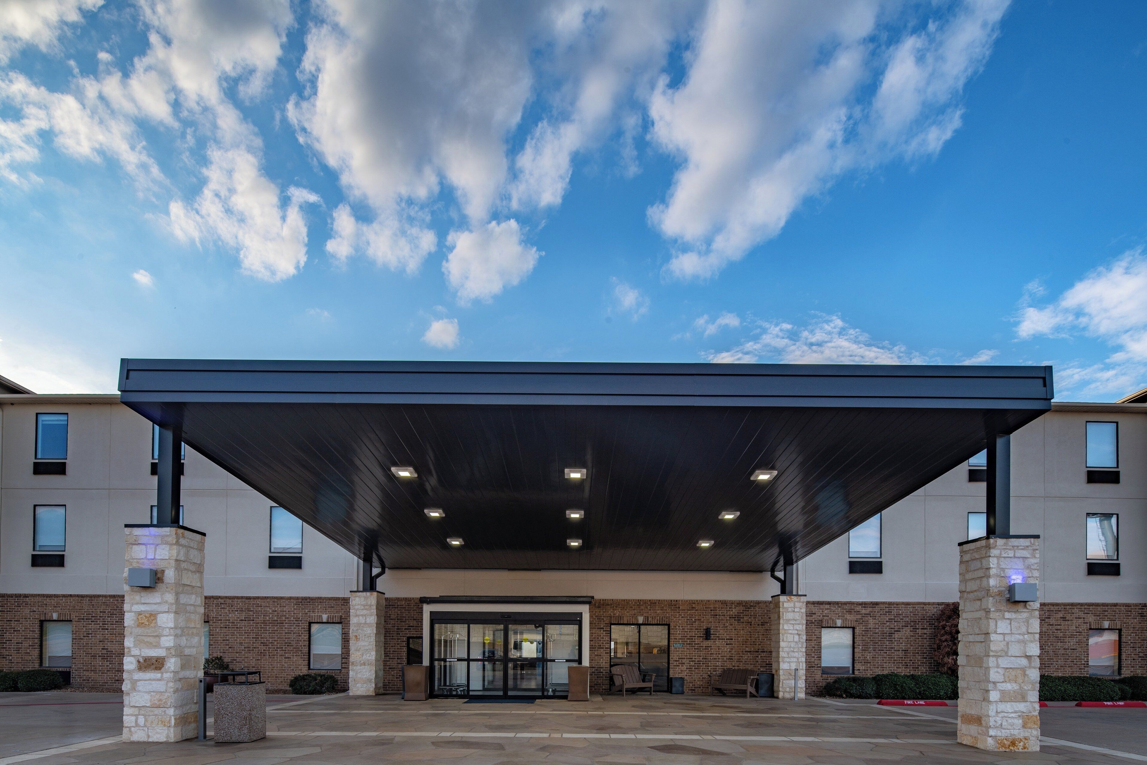 A modern building with a covered entrance, stone pillars, and a clear sky.