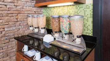 Una barra de desayuno con dispensadores de cereales, cafeteras y una pila de vasos desechables.
