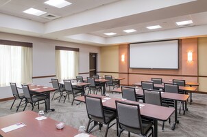 Un salón de conferencias con varias mesas y sillas, una pantalla de proyector y suelo alfombrado.