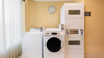 Een wasruimte met een voorlader wasmachine, een droger met bovenin zitplaats en een gestapelde droger. Een klok hangt aan de muur.