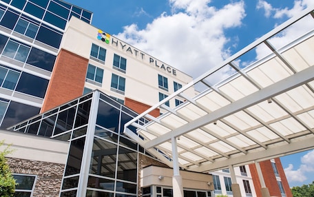 A modern hotel with a glass facade, a covered entrance, and a clear sky.