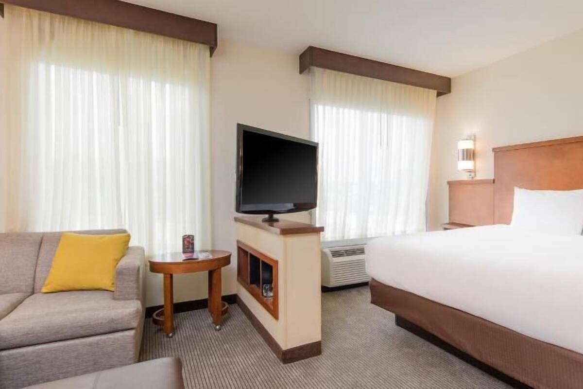 A hotel room with a bed, a TV, a sofa, and a small table.