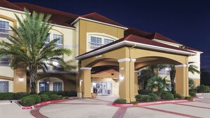 Um hotel com telhado de telhas vermelhas, entrada coberta e uma palmeira em primeiro plano.
