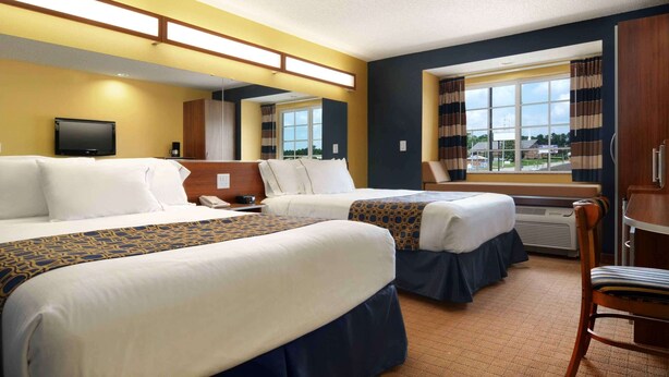 A hotel room with two beds, a TV, a desk, and a window with curtains. - Microtel Inn & Suites by Wyndham Columbus/Near Fort Benning (Columbus)