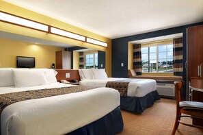 Habitación de hotel con dos camas, televisión, escritorio y ventana con cortinas.