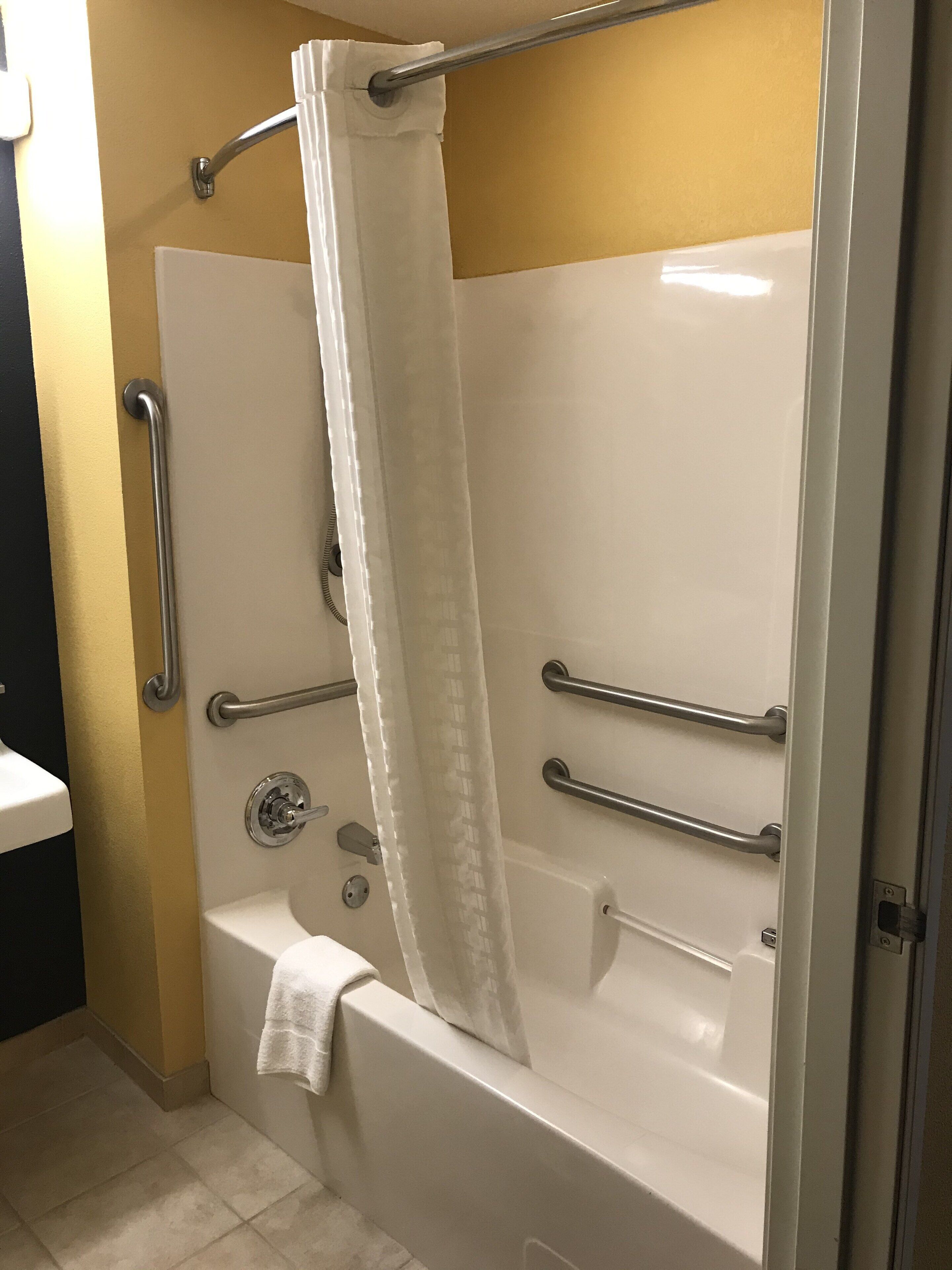 A walk-in shower with a white bathtub, grab bars, and a shower curtain.