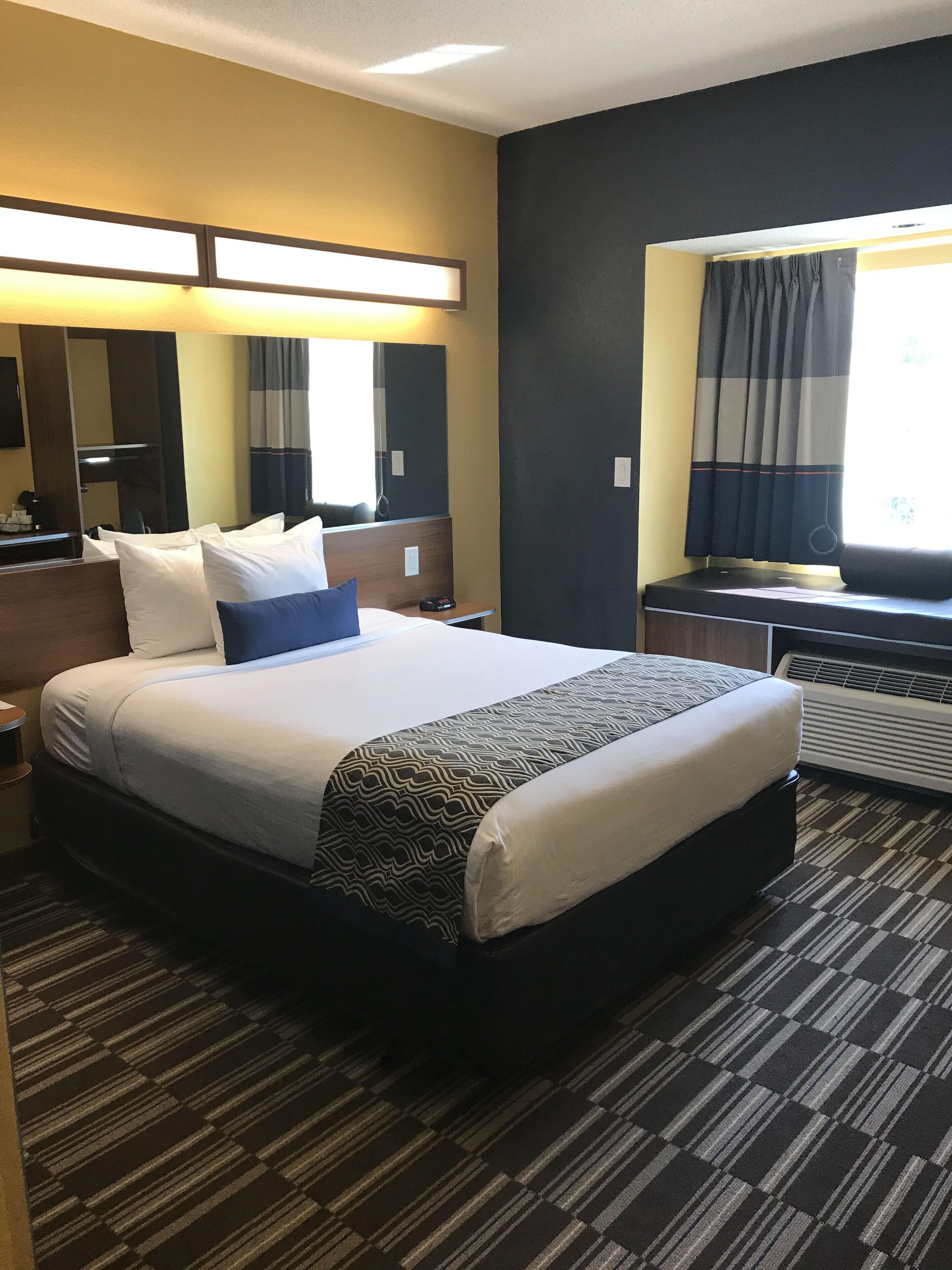 A hotel room with a large bed, a desk, a chair, a mirror, and a window with curtains.