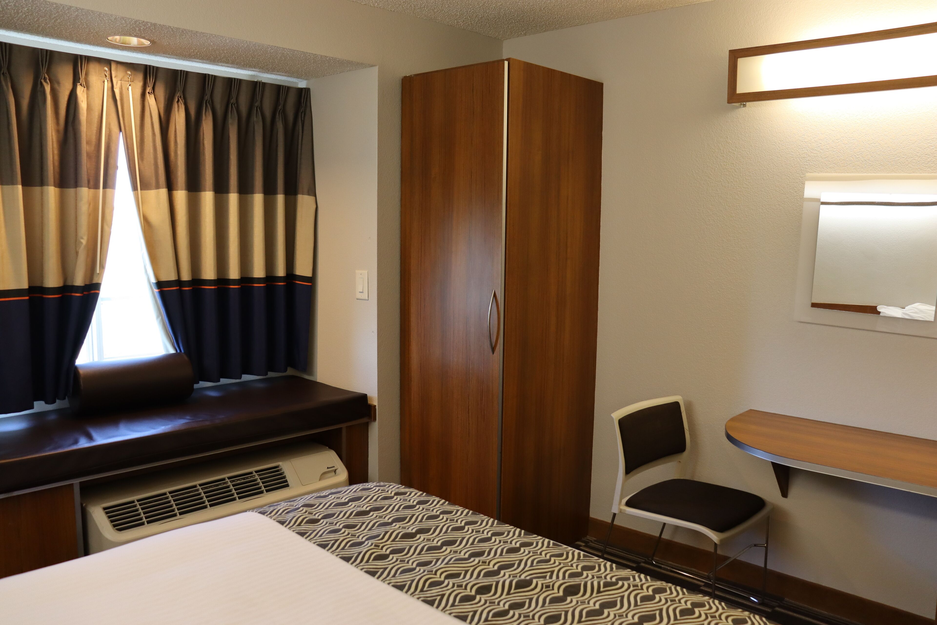Une pièce comprenant un lit, une armoire en bois, un bureau avec une chaise et une fenêtre avec des rideaux.