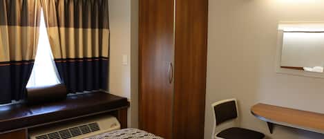 A room with a bed, a wooden wardrobe, a desk with a chair, and a window with curtains.