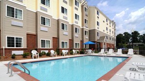 A swimming pool with lounge chairs and a building with multiple windows and balconies. - Microtel Inn & Suites by Wyndham Columbus/Near Fort Benning (Columbus)