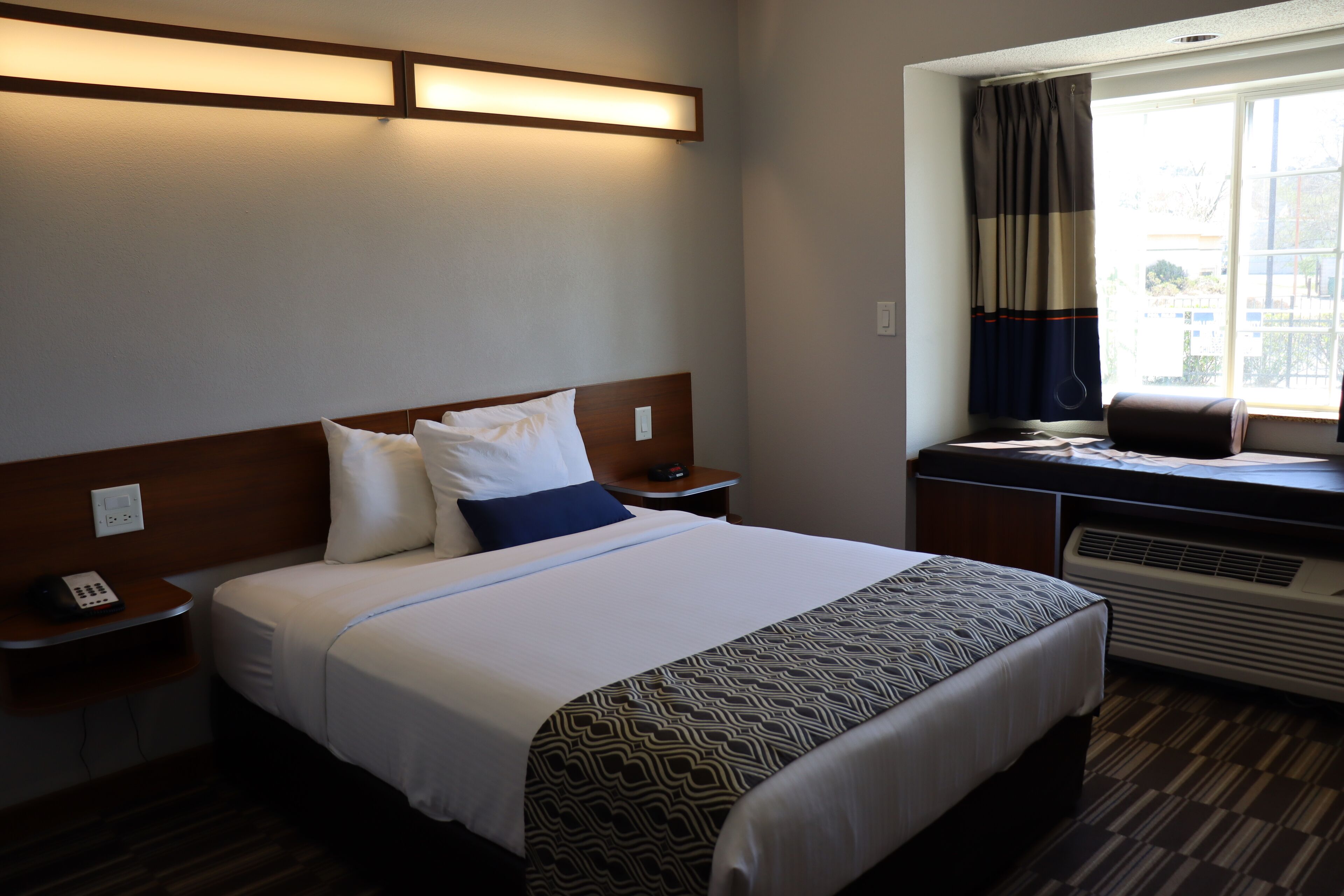 A hotel room with a bed, bedside tables, a desk, and a window with curtains.