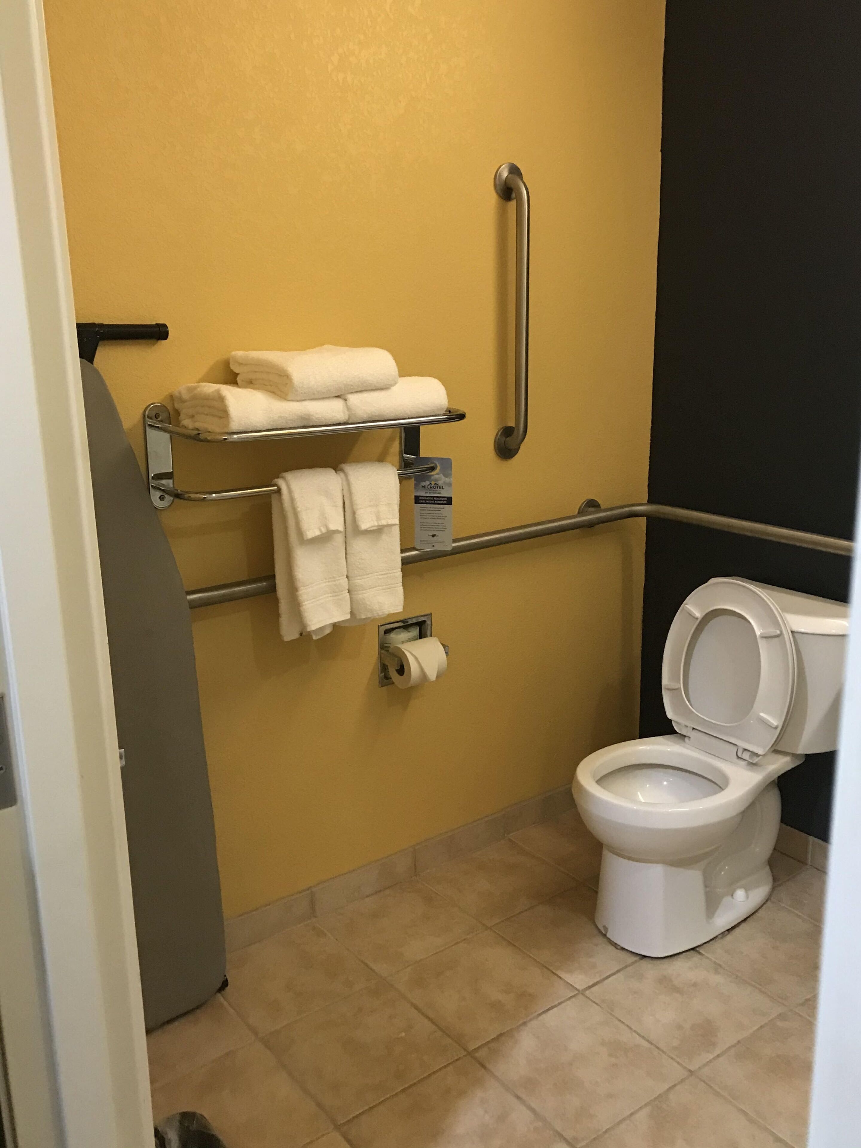 Uma casa de banho pequena com sanita, um apoio para a mão, um porta-toalhas com toalhas e um dispensador de papel higiénico.