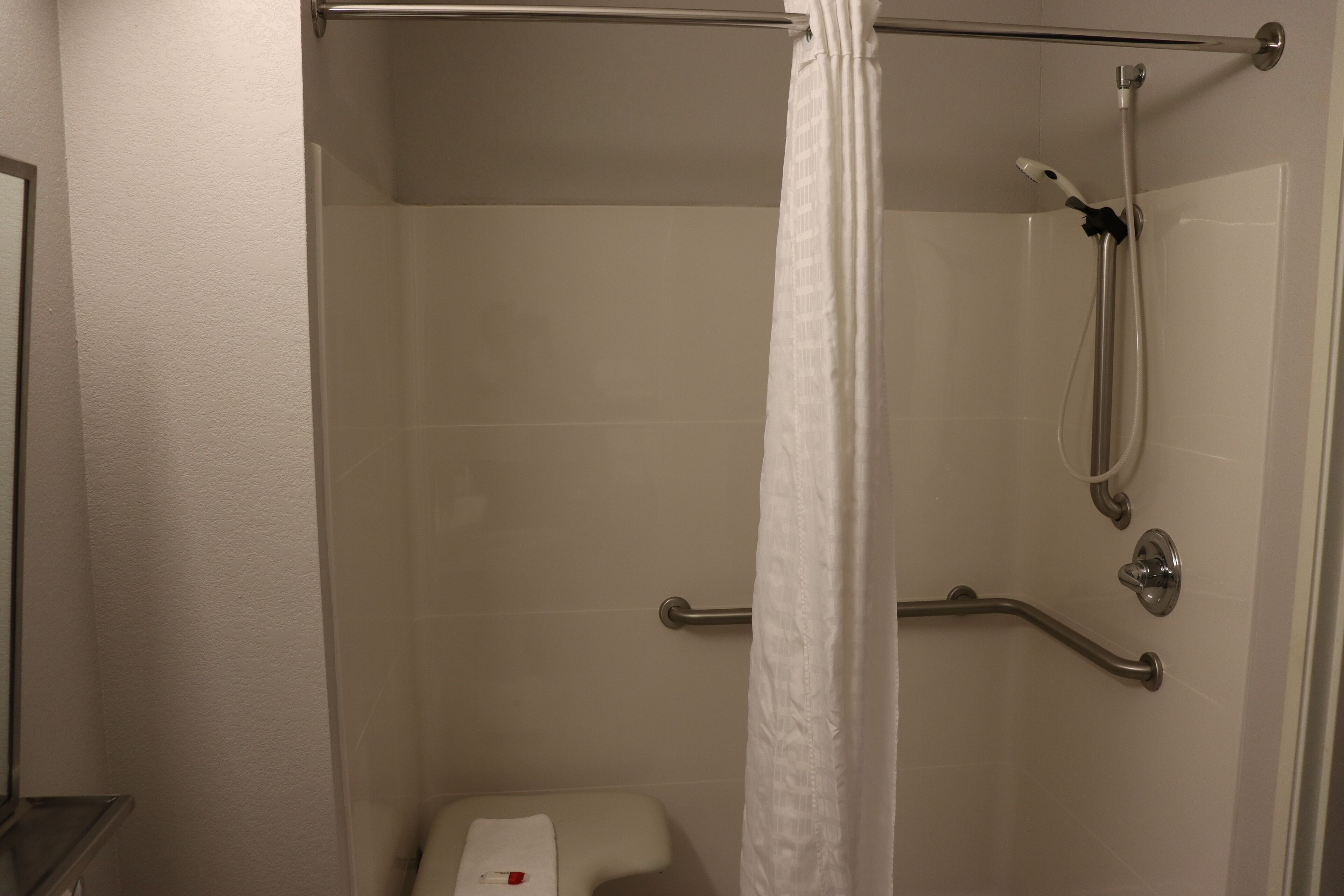 A shower area with a glass door, a handheld showerhead, and a grab bar.