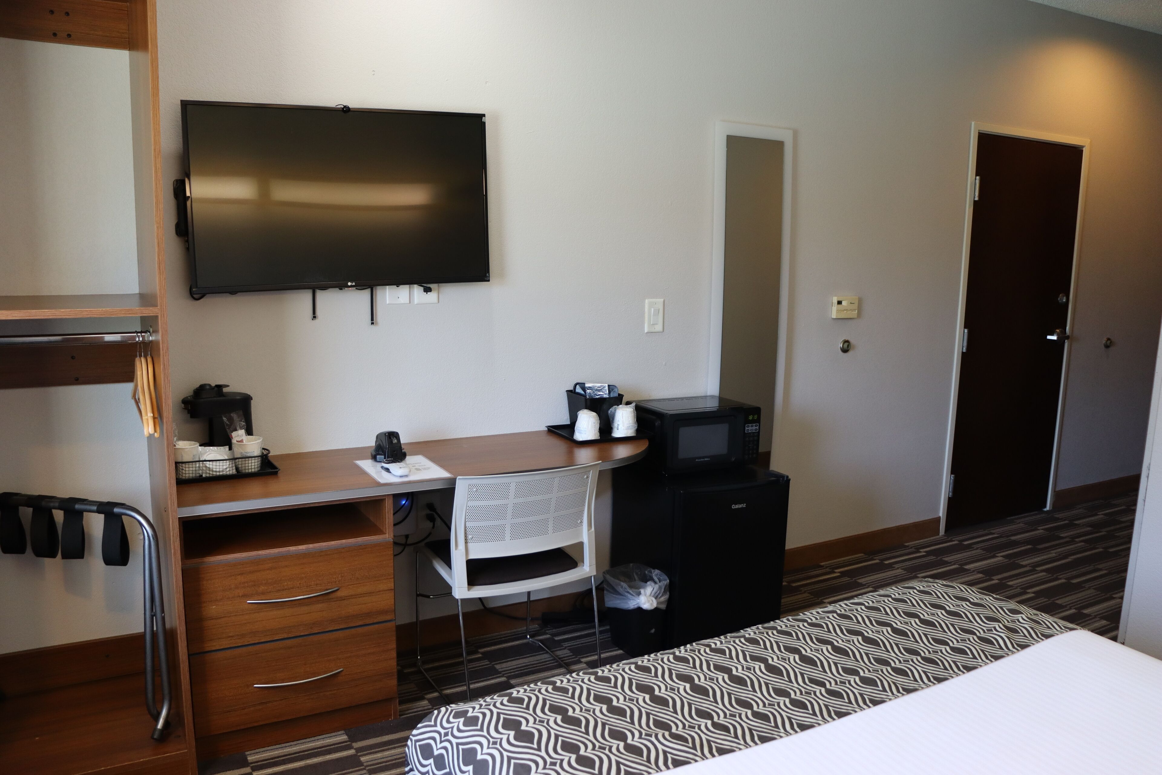 A hotel room with a bed, a desk with a computer, a microwave, and a small refrigerator.