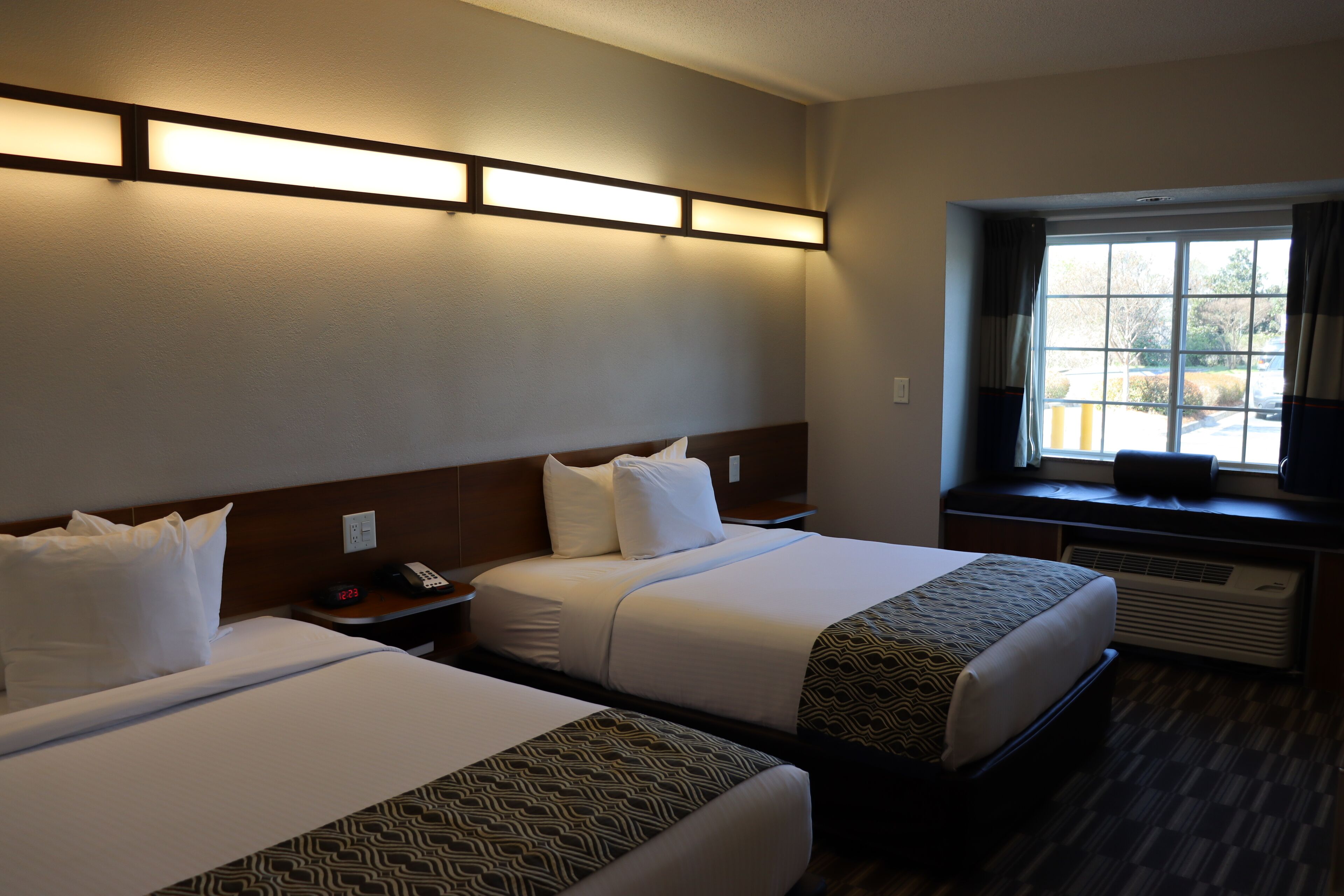 Habitación de hotel con dos camas, una mesita de noche con teléfono, una ventana con cortinas y un equipo de aire acondicionado.