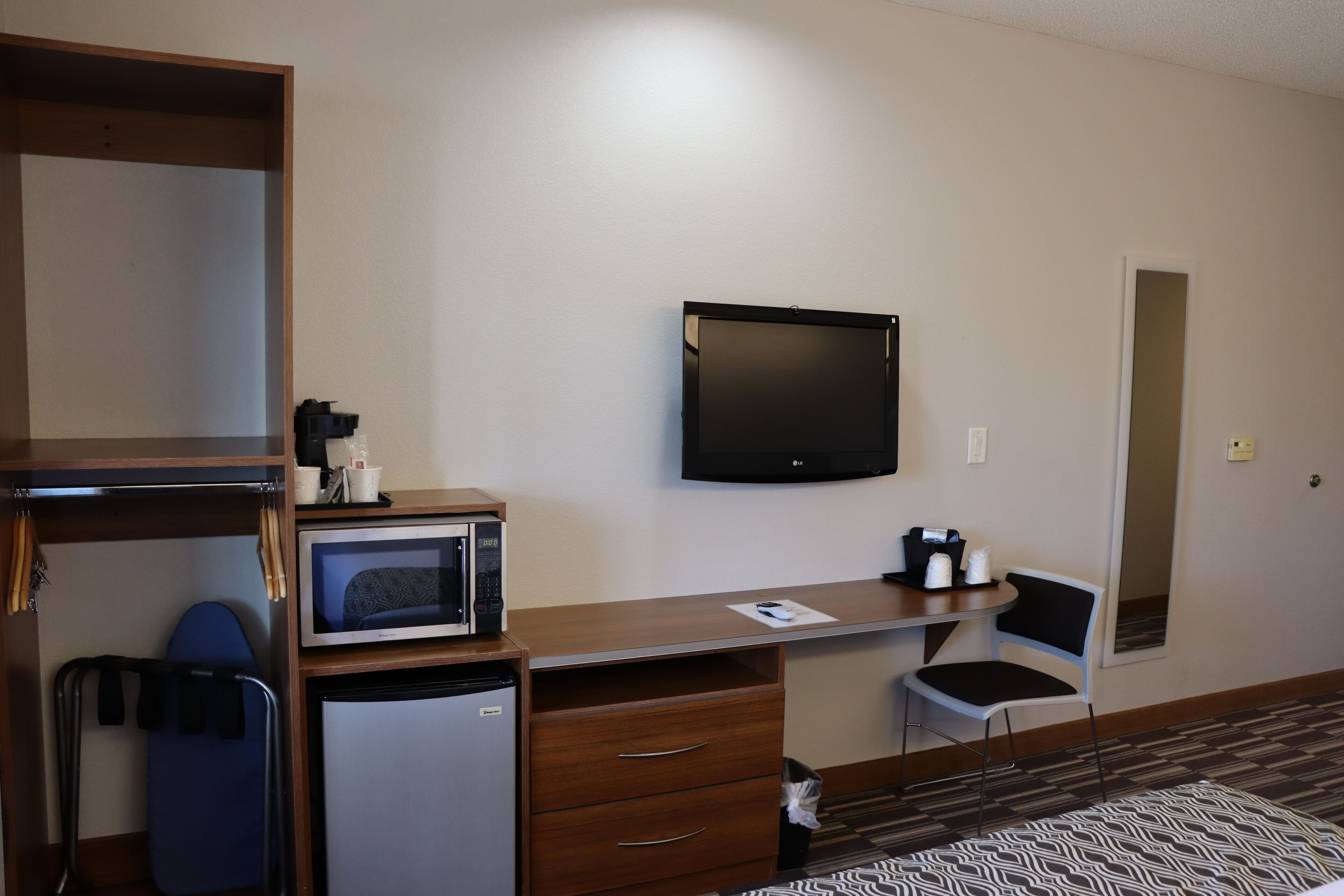 Une chambre d’hôtel équipée d’un bureau, d’un four à micro-ondes, d’un réfrigérateur, d’une télévision, d’une chaise et d’une petite poubelle.
