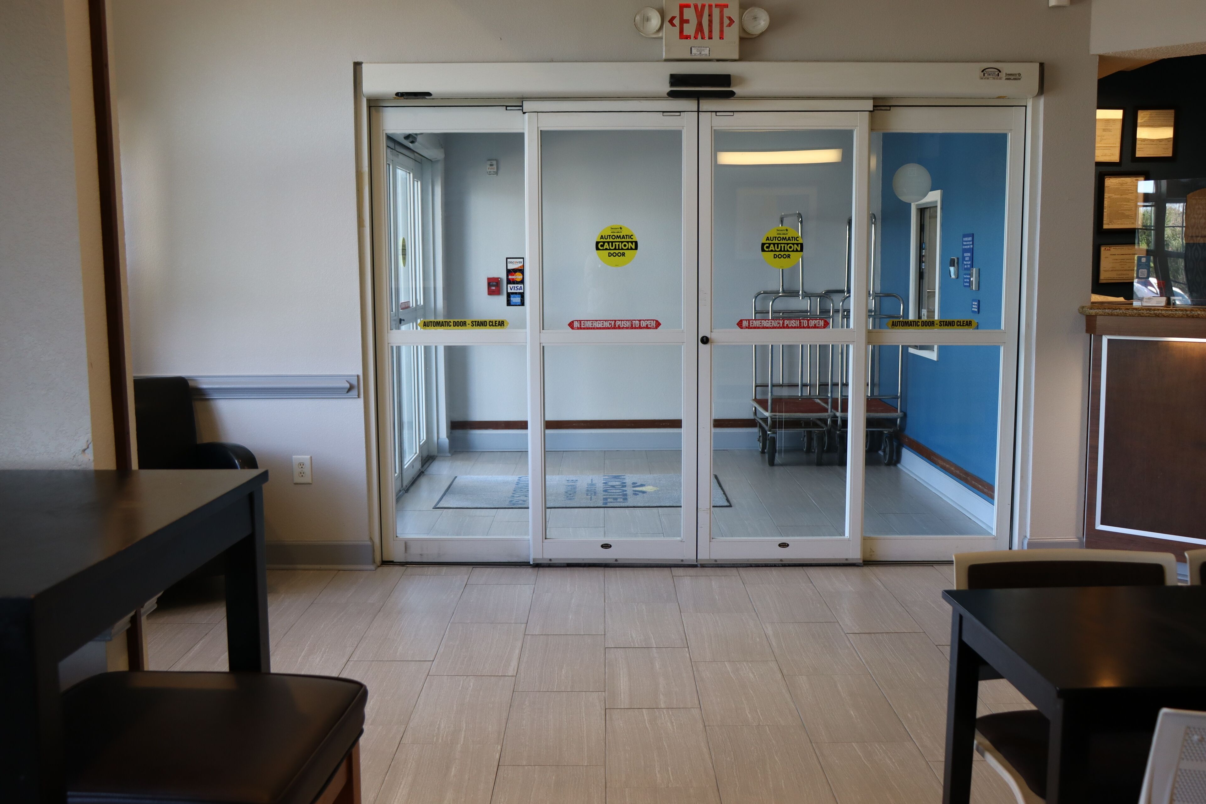 A hotel entrance with automatic caution doors, a clear exit sign, and a view into the interior.