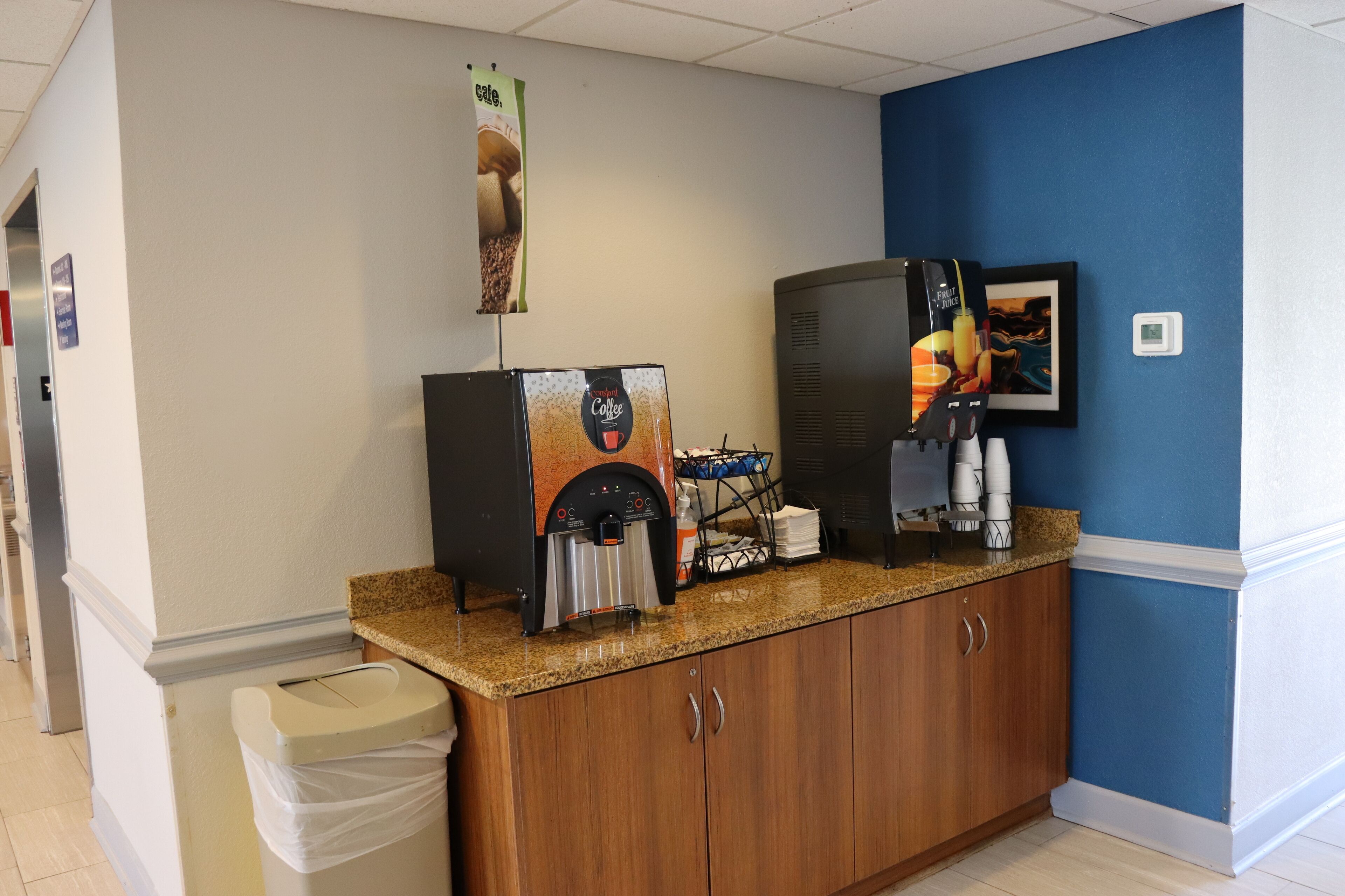 A coffee station with two espresso machines, a trash bin, and a coffee dispenser.
