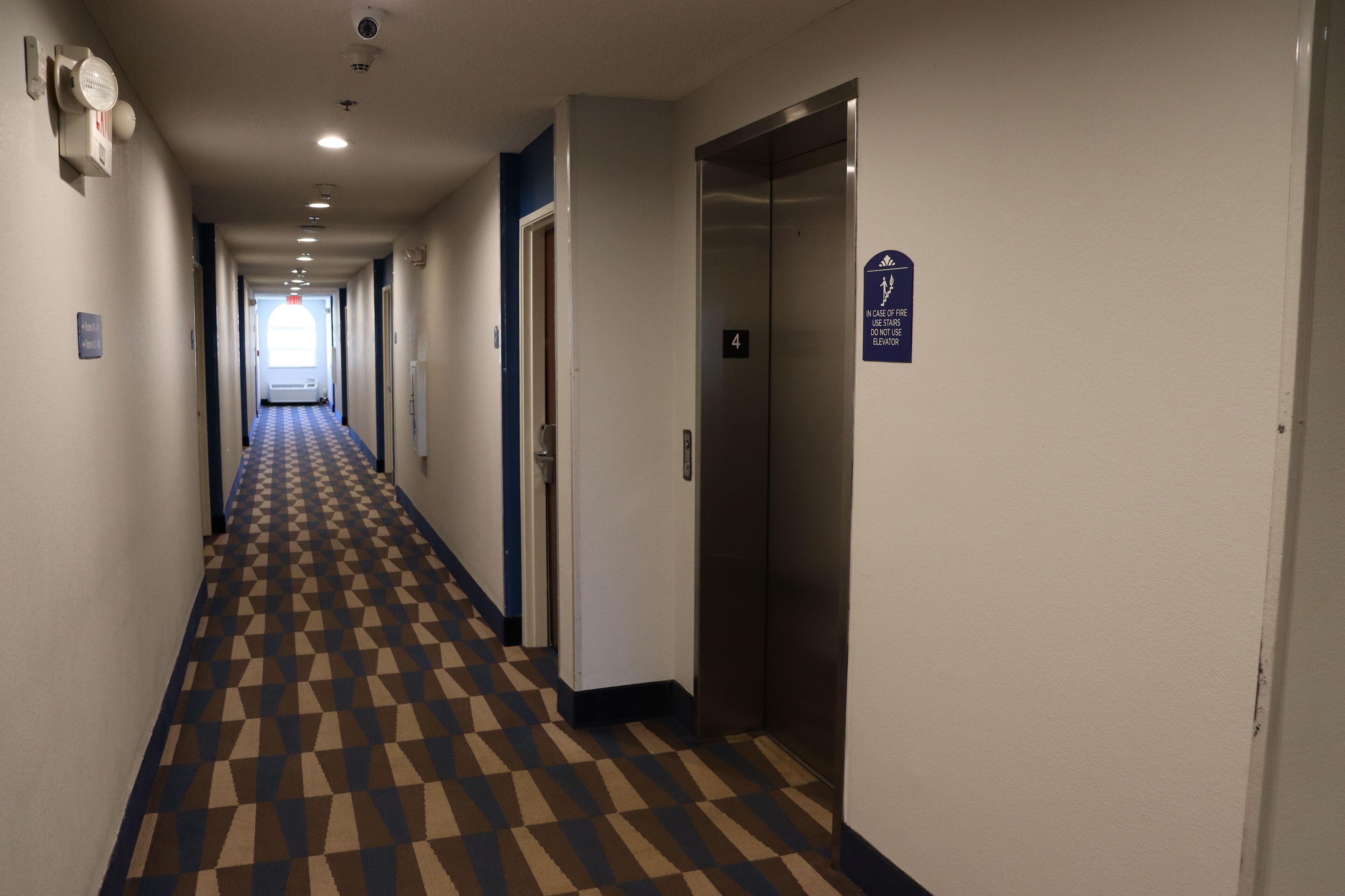 A hotel hallway with a checkered floor, an elevator, and a door with a sign.