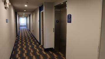 A hotel hallway with a checkered floor, an elevator, and a door with a sign.