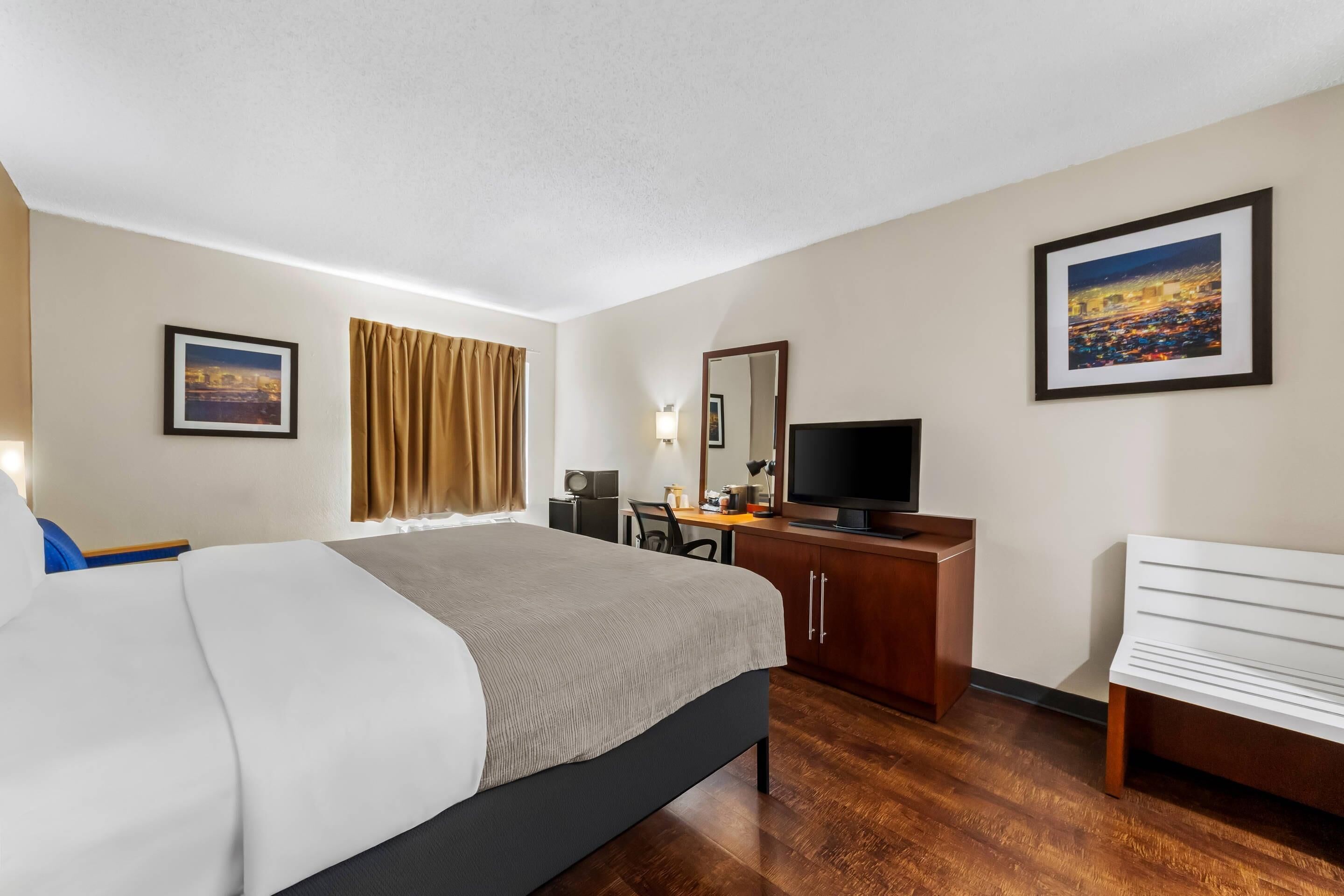 Una habitación de hotel con cama, escritorio, televisor y una banca.