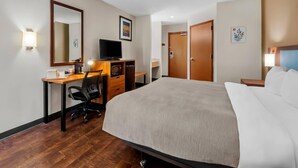 A hotel room with a bed, desk, chair, TV, and a door.