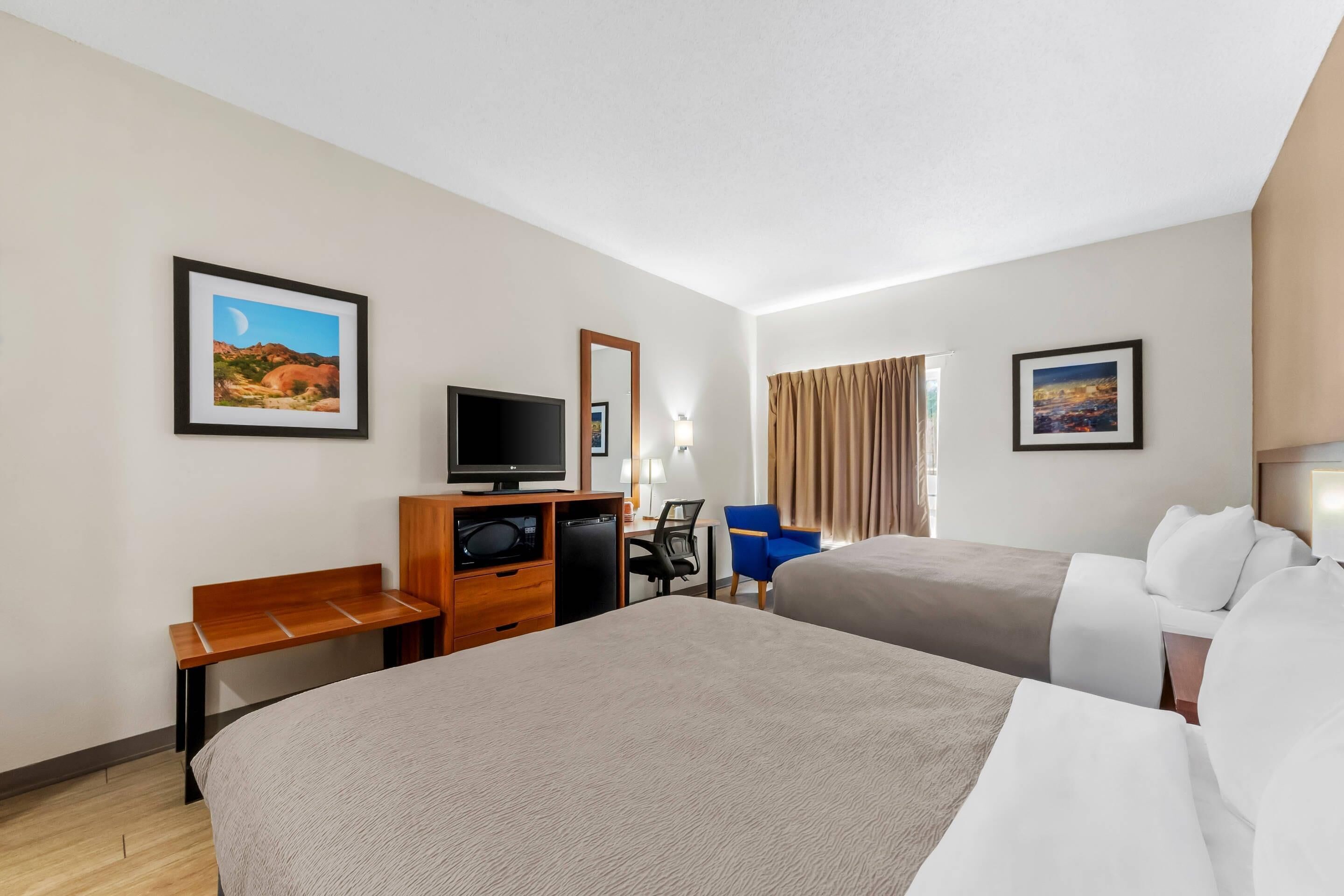 Une chambre d’hôtel avec deux lits, un bureau avec un ordinateur, une télévision et une chaise.