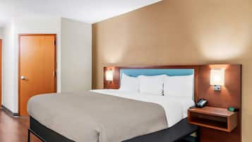 A hotel room with a bed, bedside table, lamp, and a door.