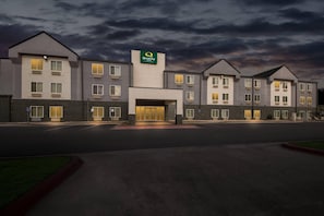 A multi-story hotel with a prominent 'Quality' sign, a central entrance, and a parking lot.