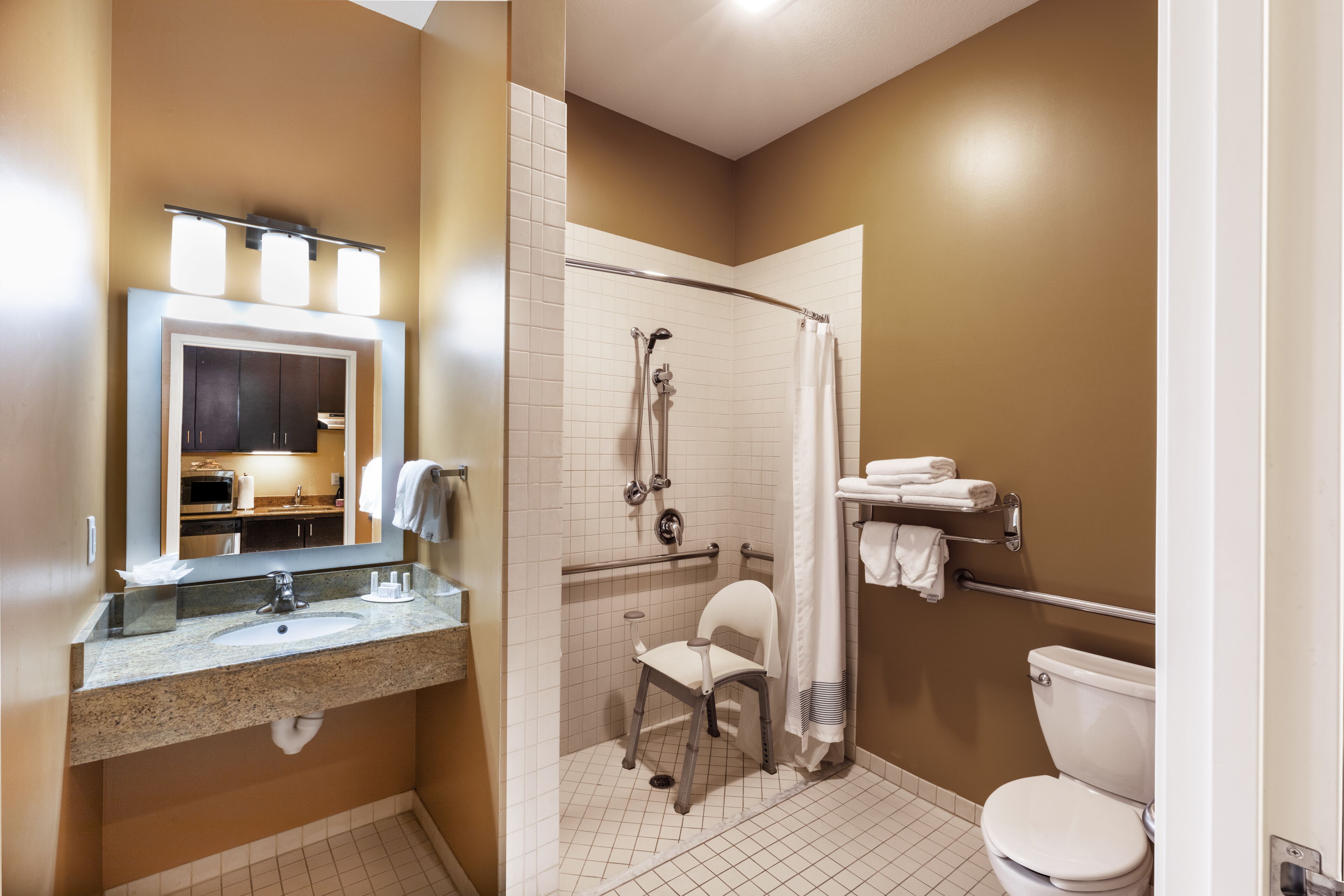 A bathroom with a sink, mirror, shower, toilet, and a chair.