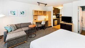 Een moderne hotelkamer met een bank, een klein rond tafeltje, een bureau, een televisie en een kitchenette.