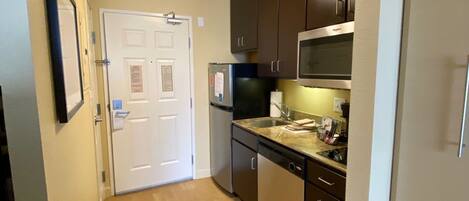 A compact kitchen with dark cabinets, a microwave, a refrigerator, and a dishwasher.