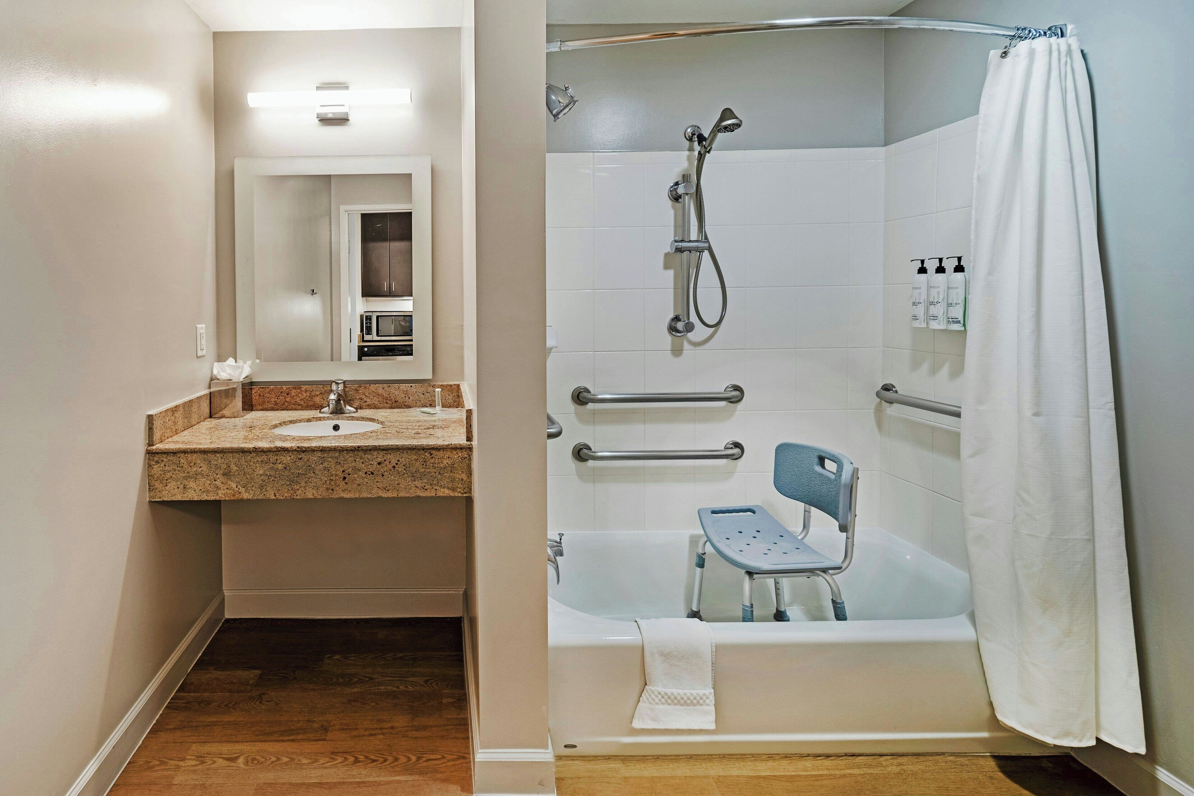 A bathroom with a sink, mirror, shower, and a wheelchair-accessible tub.