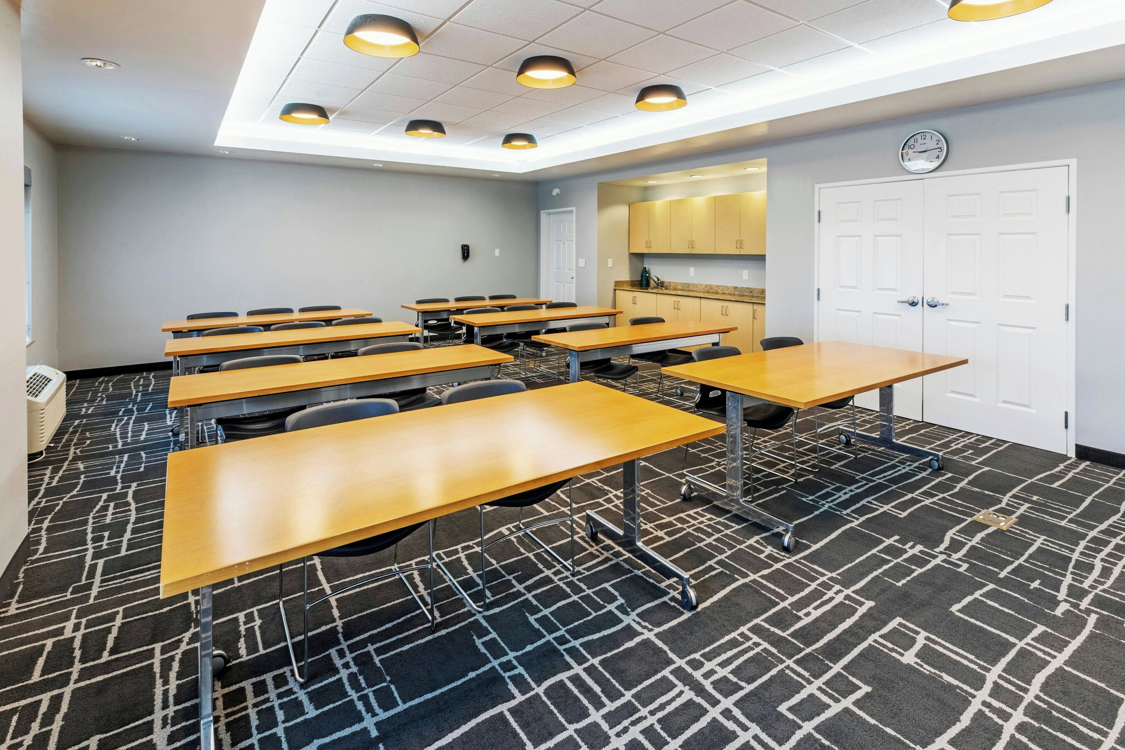 A conference room with multiple tables and chairs, a clock on the wall, and a kitchenette area.