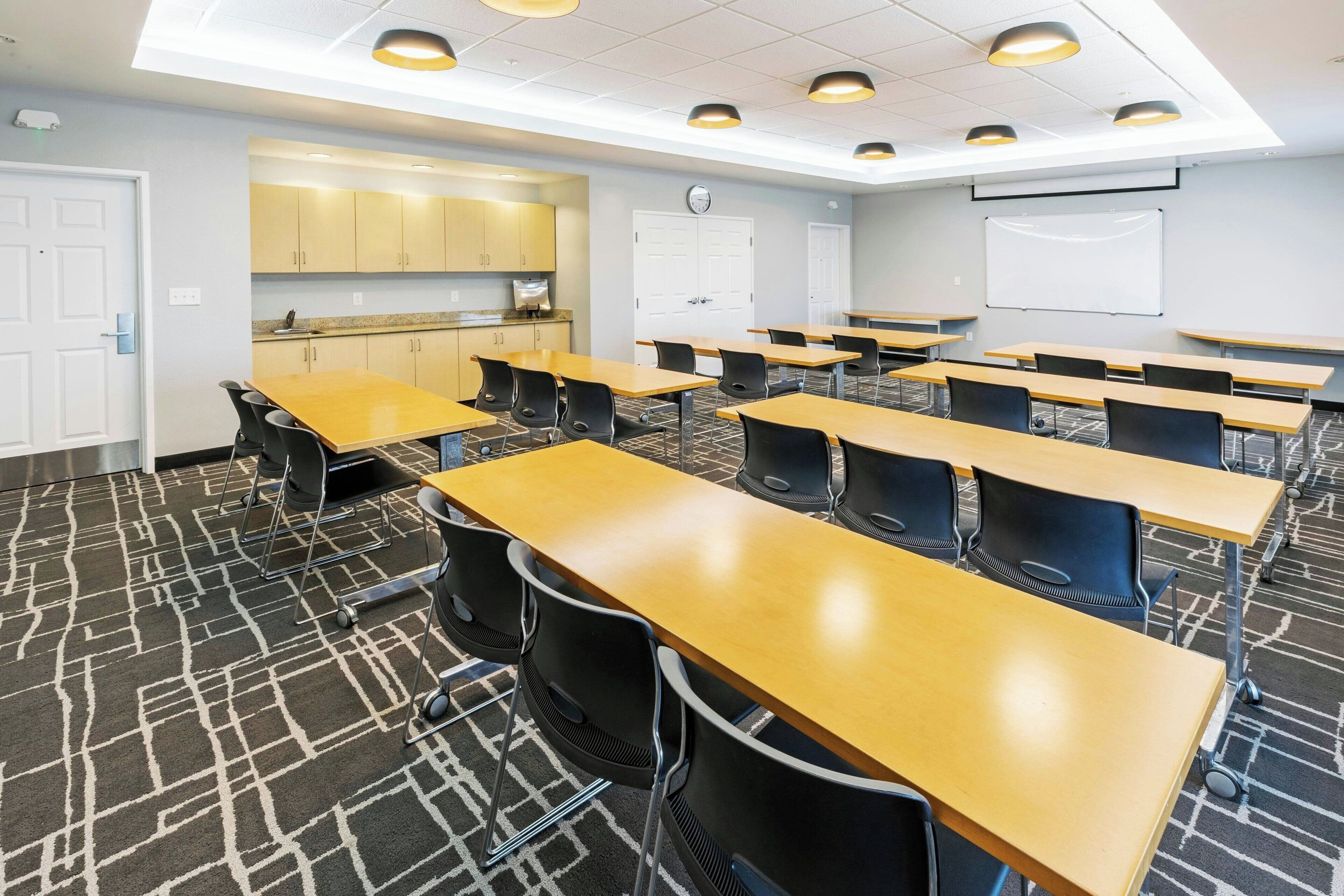 A classroom with rows of desks, a whiteboard, and a kitchenette area.