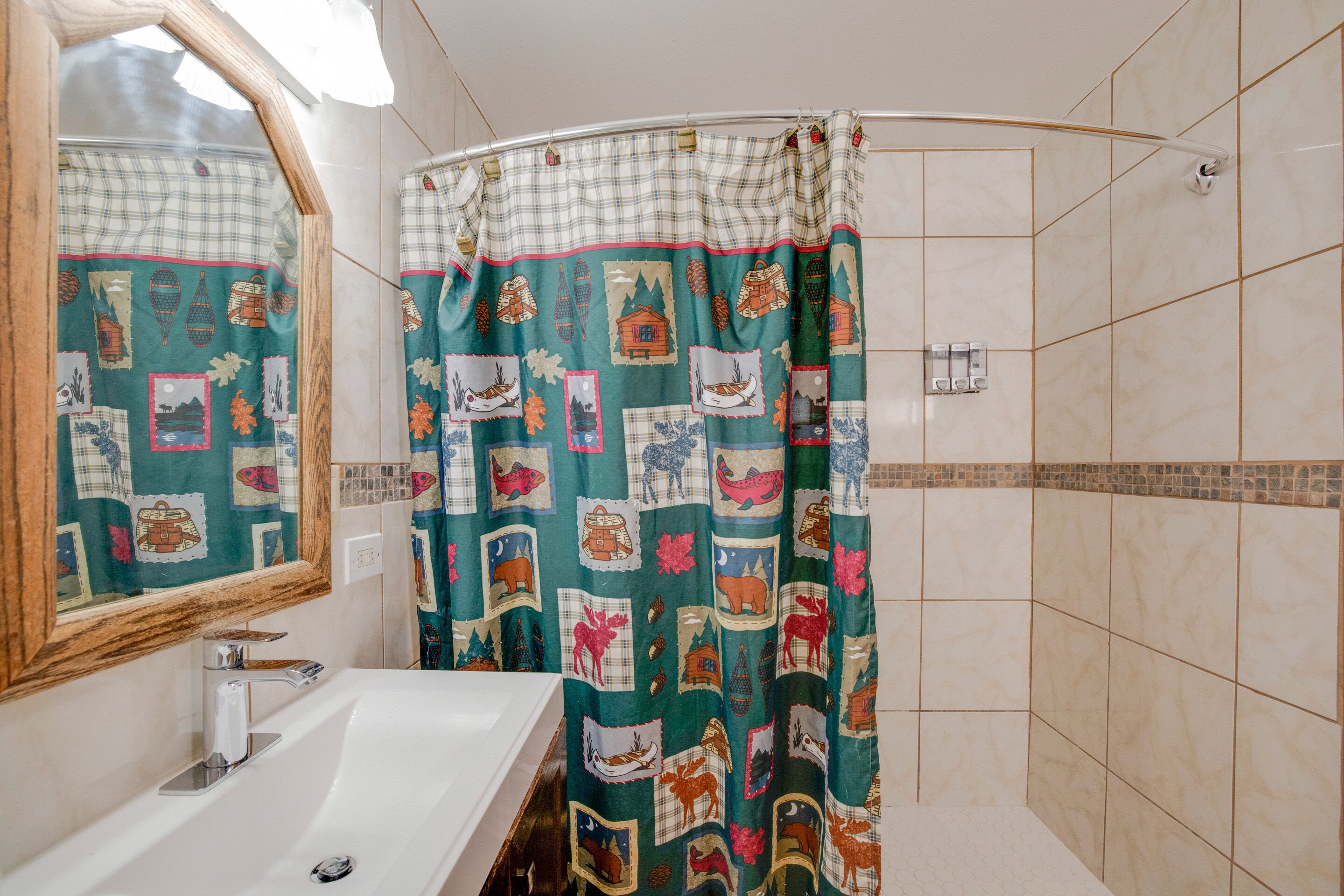 Une salle de bain avec un lavabo blanc, un miroir et un rideau de douche orné d’un motif représentant des animaux sauvages.