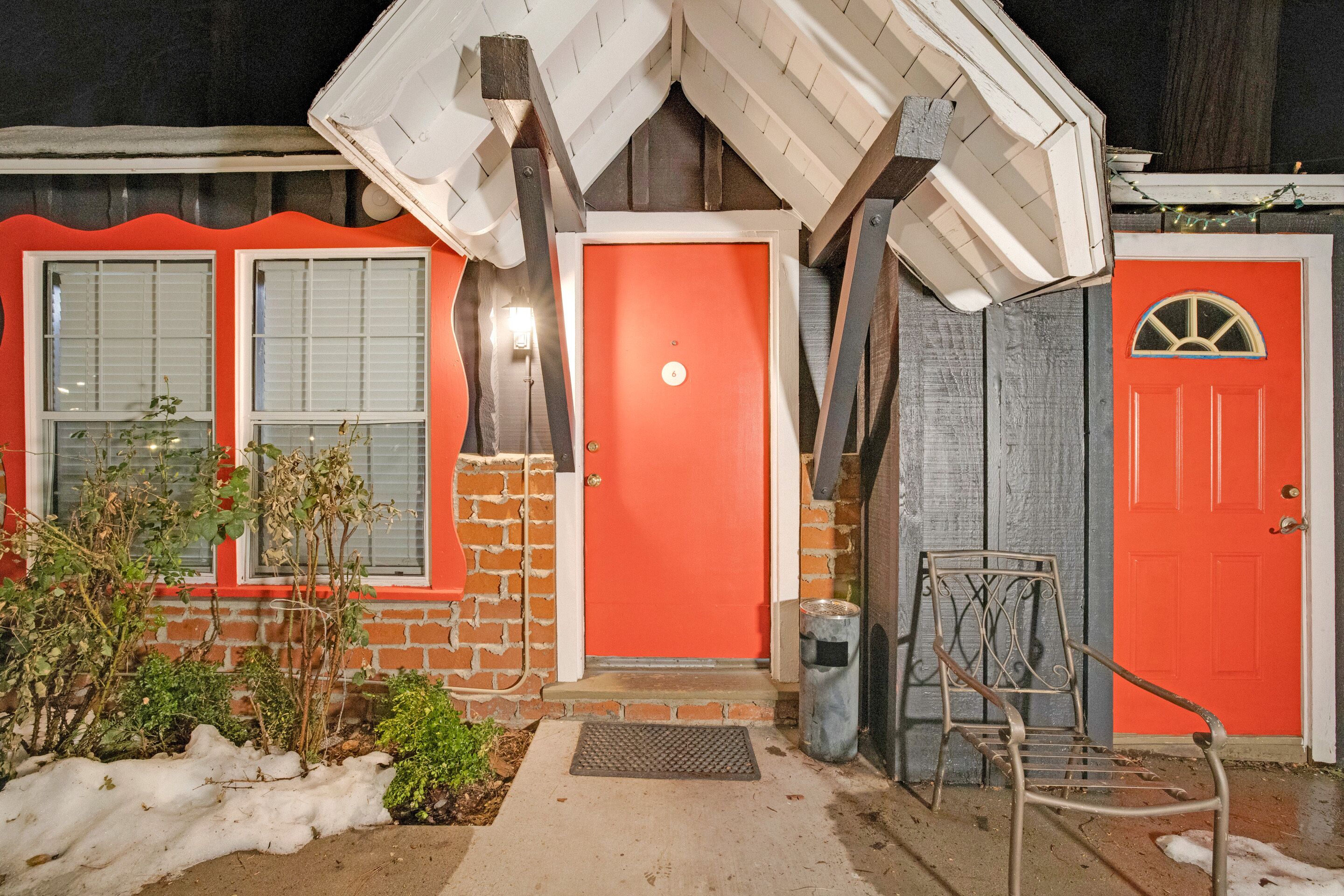 A house with a red door, a metal chair, and a trash can in the front yard.