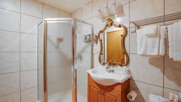 A bathroom with a glass-enclosed shower, a white sink, a wooden vanity, a mirror with an ornate frame, and a towel rack with white towels.