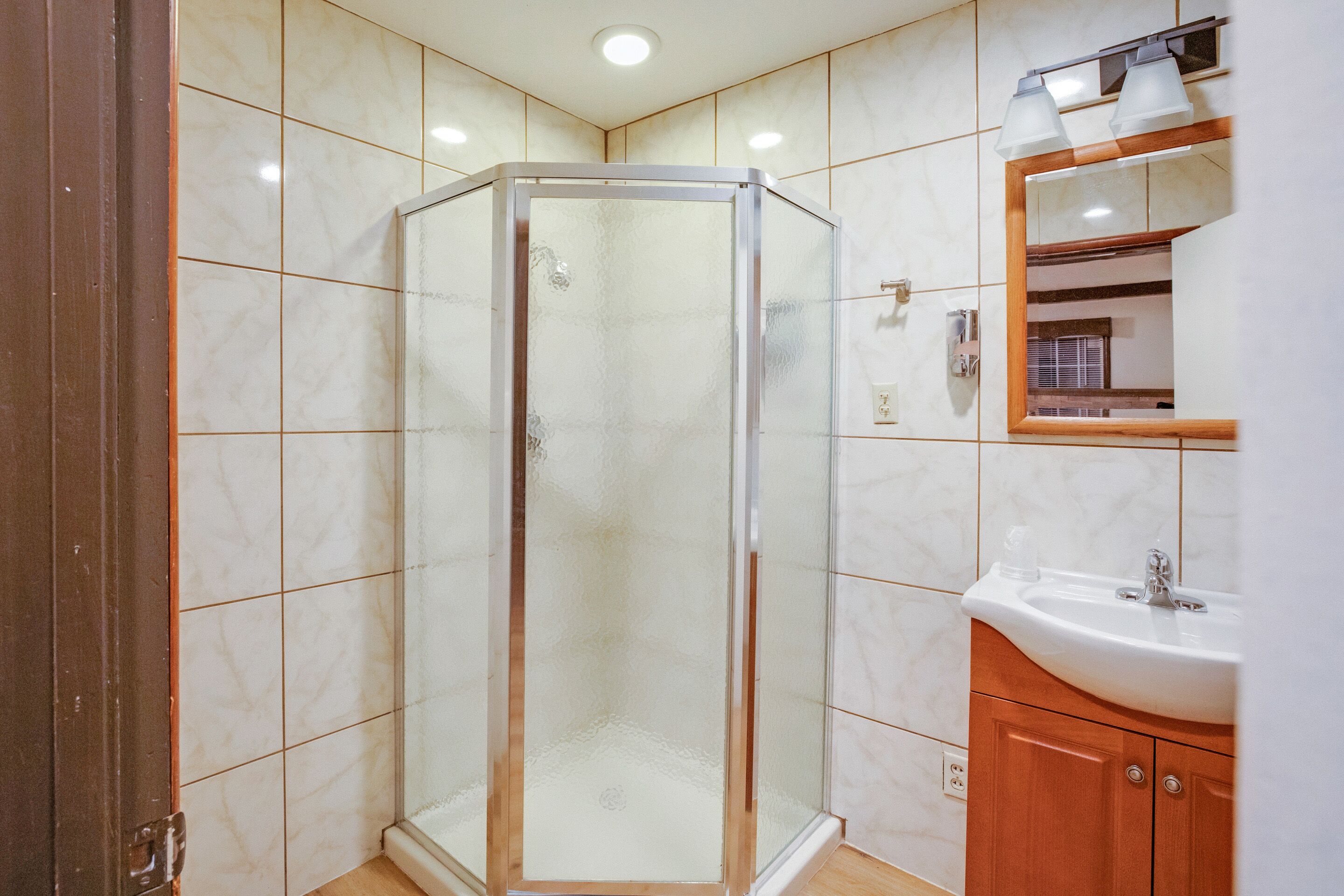 Ein Badezimmer mit einer Duschkabine, einem Waschbecken mit Spiegel und gefliesten Wänden.