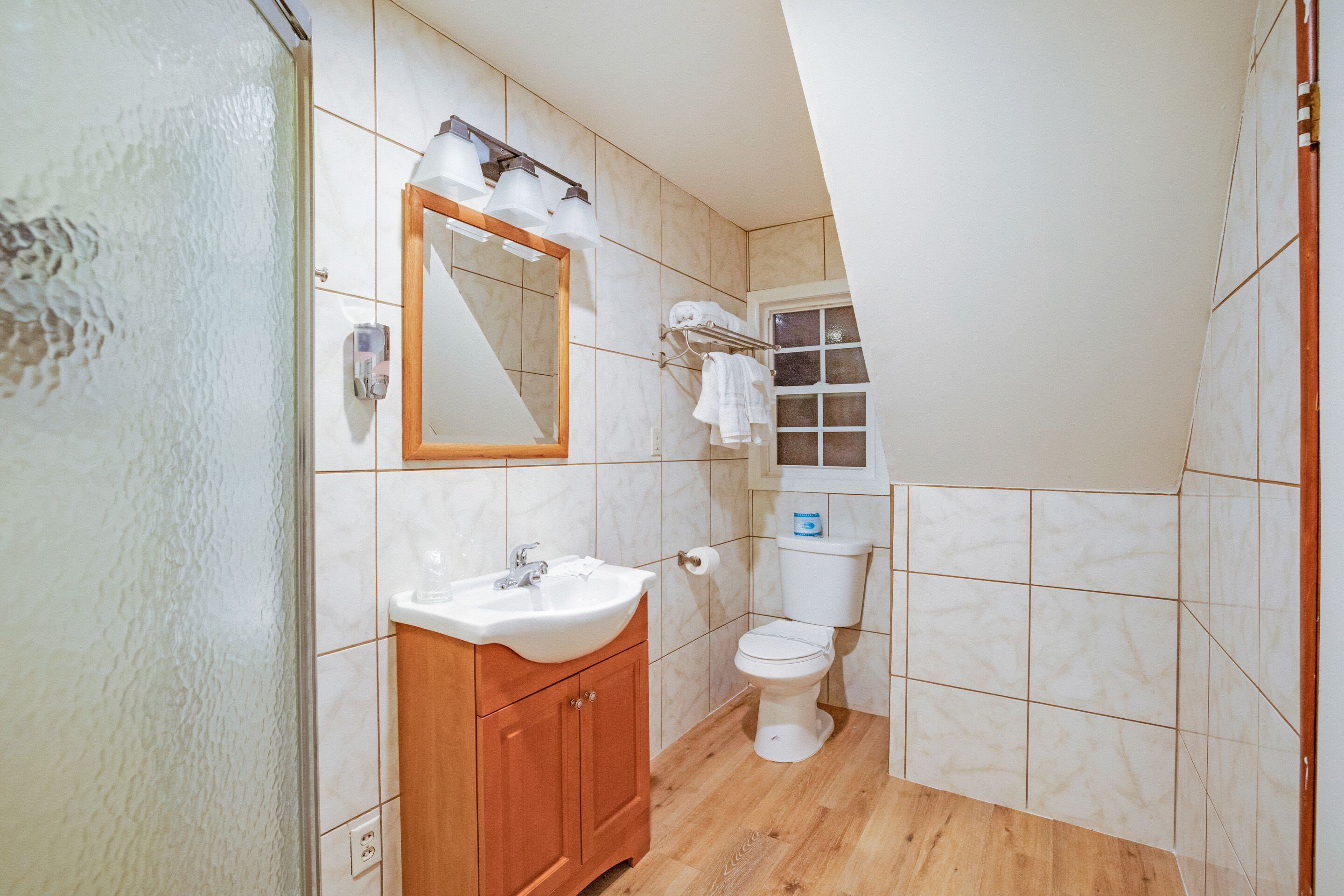 Ein Badezimmer mit Holzwaschtisch, Spüle, Spiegel, Toilette und einem Fenster mit Milchglas.