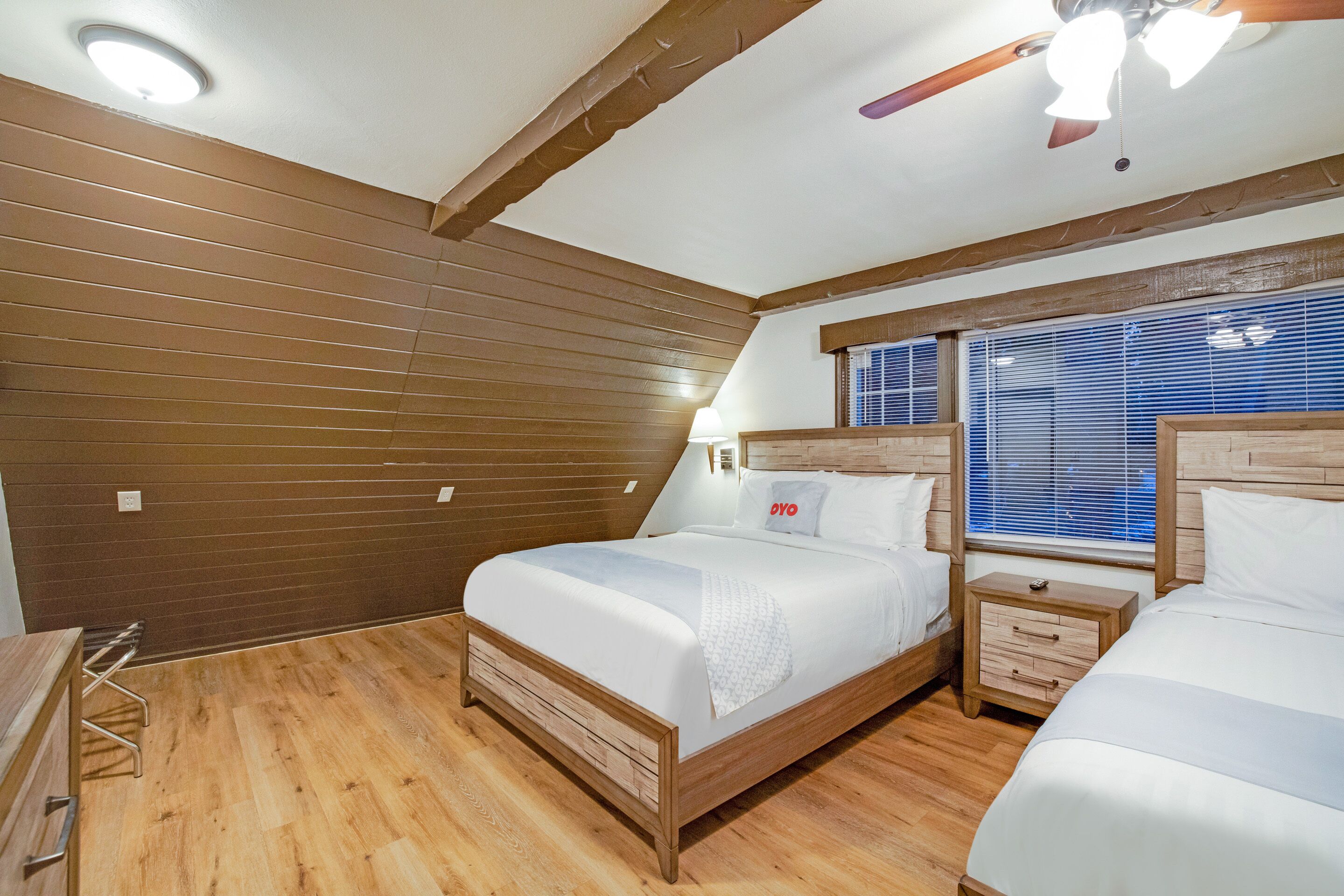 Ein Schlafzimmer mit zwei Betten, Holzwänden, einem Deckenventilator und einem Fenster mit Jalousien.