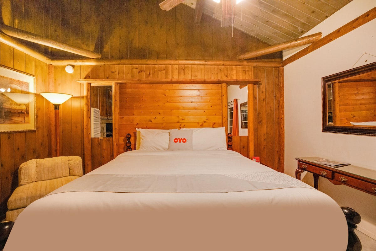 Une pièce aux murs lambrés, avec un grand lit, une chaise, une table et un miroir accroché au mur.