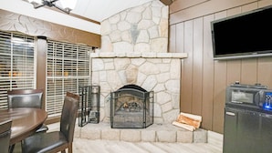 A stone fireplace with a TV above it, a dining table with chairs, and a microwave to the right. - Arrowhead Tree Top Lodge (Lake Arrowhead)
